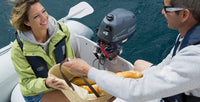 Yamaha 4 PK buitenboordmotor gemonteerd op een rubberboot, terwijl twee personen ontspannen varen en een mand met eten overhandigen op het water.